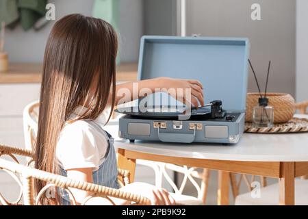 Little girl with record player at table in kitchen Stock Photo