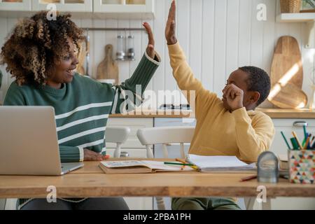 Happy African American mother and son giving each other high fives while studying together at home Stock Photo