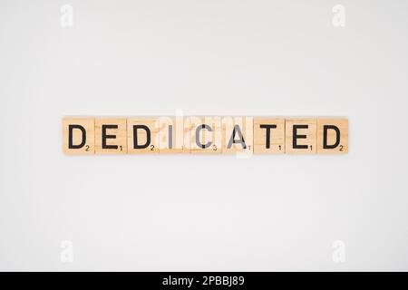 Wooden title spelling the word dedicated isolated on a white background Stock Photo