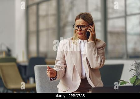 Focused professional enterprier talking by phone with client while sitting in modern office Stock Photo