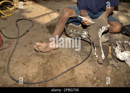 A villager uses a cleaner as he is working with a fossilized bone of