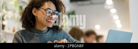 Smiling african woman speaks sign language with friends by video call while sitting in cozy cafe Stock Photo