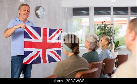 Male professor shows adult students flag of Great Britain. History professor talks about formation of state of Great Britain Stock Photo