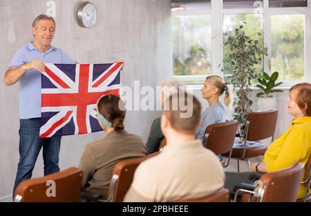 Male professor shows adult students flag of Great Britain. History professor talks about formation of state of Great Britain Stock Photo