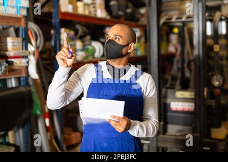 Worker in protective mask taking inventory in building materials store Stock Photo