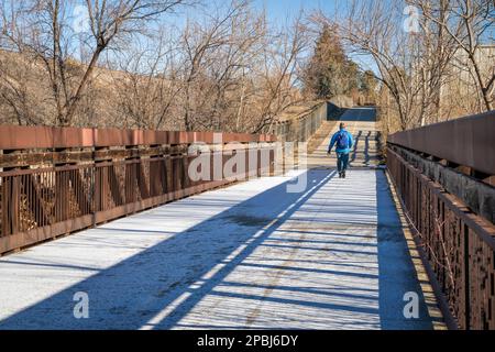 older man with a backpack is walking on a biking trail and footbridge covered by frost, winter morning in Fort Collins, Colorado Stock Photo