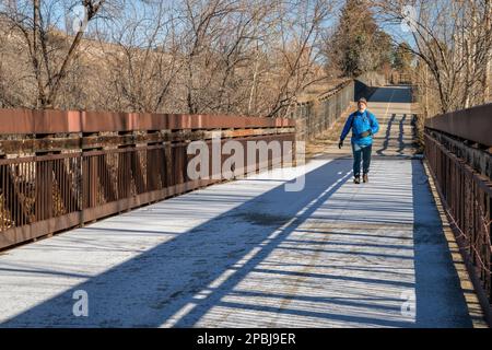 older man with a backpack is walking on a biking trail and footbridge covered by frost, winter morning in Fort Collins, Colorado Stock Photo