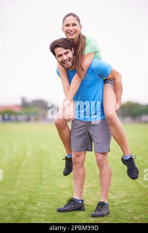 We always have fun together. a young man playfully carrying his girlfriend on his back while working out. Stock Photo