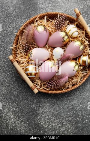 Golden and pink colored eggs and  feathers in wicker plate on a dark concrete background Stock Photo