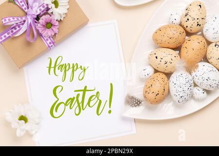 Easter eggs, flowers and gift box over beige background. Flat lay with easter greeting card Stock Photo