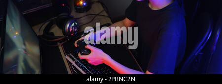 Female cyber hacker gamer playing or streaming video games on computer with joystick in neon light. Stock Photo