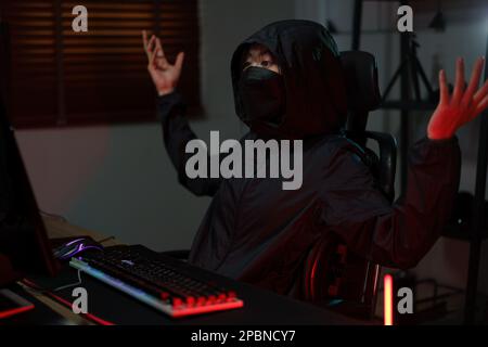 Hacker in hoodie raising hands while having problem with hacking programming system or server. Stock Photo