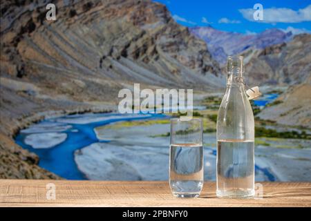 Bottle of pure water and a glass on a wooden table with the Himalayan mountains background on a sunny day, close up Stock Photo