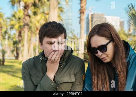 Young heterosexual couple is troubled. Boyfriend and girlfriend or wife and husband are facing problem, sitting with their heads down. Stock Photo