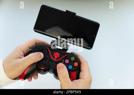 Game Pad with smartphone in hands on white background. Mobile Gaming concept. a blank white screen on a smartphone. copy space. Stock Photo