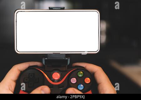 Game Pad with smartphone in hands on black background. Mobile Gaming concept. a blank white screen on a smartphone. copy space. Stock Photo
