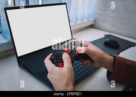 Open laptop computer with a blank white screen with copy space standing open on a table alongside a video game controller indoors at home. joystick fo Stock Photo