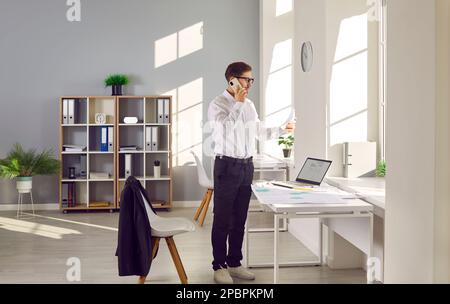 Architect or cadastre engineer standing by office desk and talking on mobile phone Stock Photo