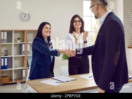 Handsome gray-haired businessman with glasses shakes hands with attractive brunette with long hair as sign of concluding good business deal. Stock Photo