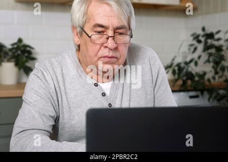Senior male business owner in glasses sitting at desk in front of laptop. Successful older male working at home. Grey haired 60s - 70s Aged busy man t Stock Photo