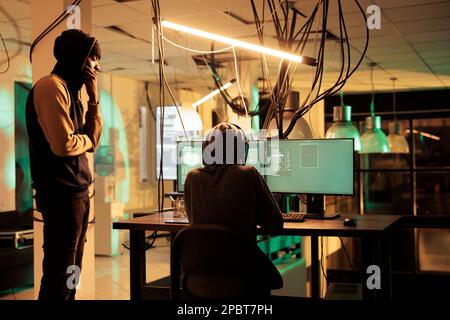 Cyberattack, criminals team coding computer virus program, hacking database, stealing electronic information. Cybercrime, data breach, hackers in hoods breaking into online server Stock Photo