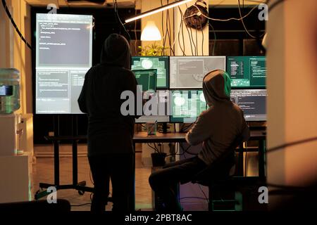 Team of two thieves using computers to break into government sensitive network, planting virus and attacking database. Young people acting dangerous hacking system at night. Stock Photo