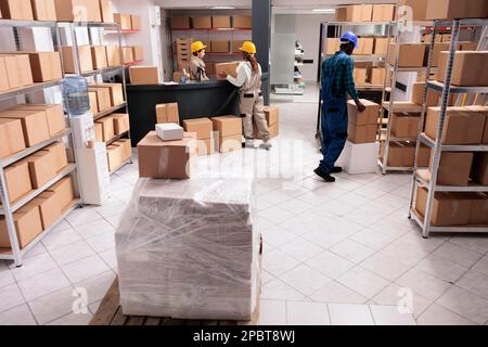 Post office storage workers managing parcels delivery, carrying and packing cardboard boxes. Logistics department employees preparing freight for distribution in industrial warehouse Stock Photo