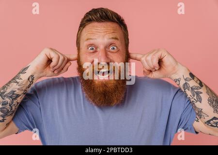 Adult redhead bearded tattooed tense man in t-shirt with clenched teeth ...