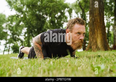 Ginger bearded man doing exercise during workout in park outdoors Stock Photo