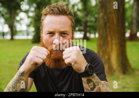 Ginger bearded man doing exercise during workout in park outdoors Stock Photo