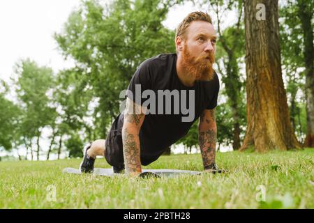 Ginger bearded man doing exercise during workout in park outdoors Stock Photo