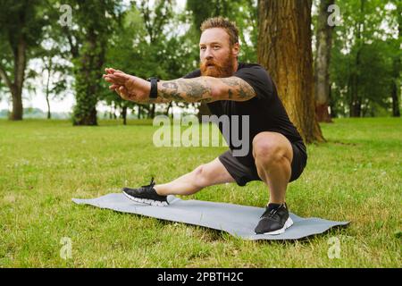 Ginger bearded man doing exercise during workout in park outdoors Stock Photo