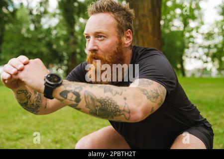 Ginger bearded man doing exercise during workout in park outdoors Stock Photo