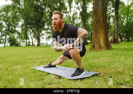 Ginger bearded man doing exercise during workout in park outdoors Stock Photo