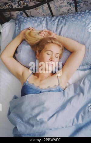 Mature middle aged woman stretching in bed waking up alone Stock Photo