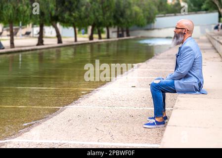 middle-aged, balding, bearded man sitting in a park relaxing Stock Photo