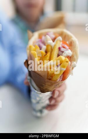 Traditional Greek gyros with pita bread, French fries, tzatziki sauce, grilled chicken meat and fresh vegetables. Unrecognizable female person holds b Stock Photo