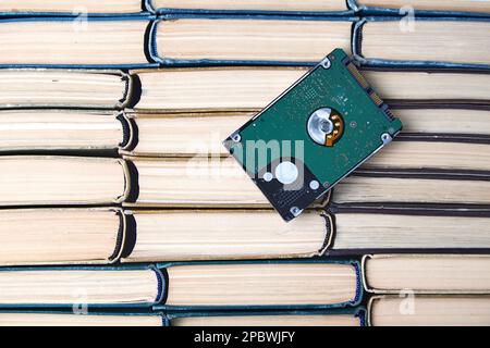 Computer hard drive on the background of a stack of old paper books. Comparison of the volumes of storage media of different eras. Top view with copy Stock Photo