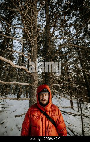 Portrait of young man in winter wearing orange puffy jacket with hood. Stock Photo