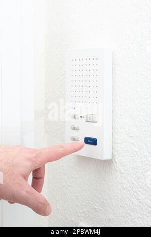 Caucasian male finger operating the intercom unit  from inside apartment. Close up interior shot, no face. Stock Photo