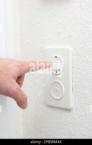 Caucasian male finger pressing the on off light switch inside apartment. Close up interior shot, no face. Stock Photo
