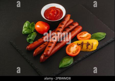 Grilled sausages on a stone background. Vegetables and sauce. Stock Photo