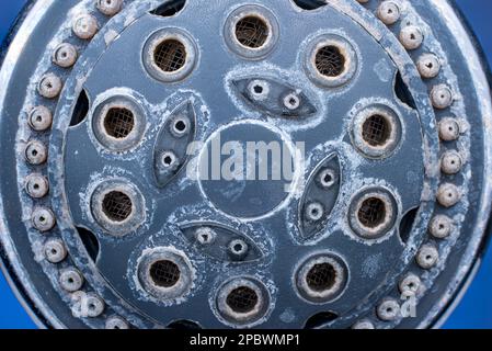 Silver metal shower head with hard water damage or lime scale calcium deposits. Close up studio macro shot, isolated on blue background. Stock Photo