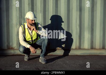 Engineer or worker sit close to cargo container look like tired and serious after work in workplace area. Stock Photo