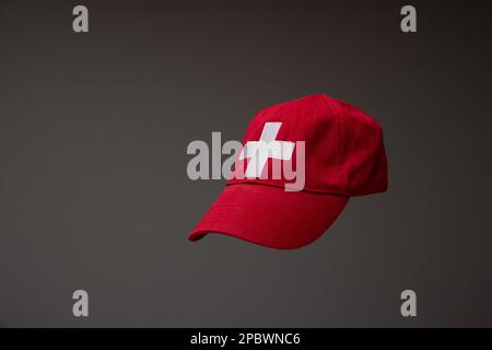 Red baseball cap with Swiss flag white cross. Close up studio shot, isolated on gray background. Stock Photo