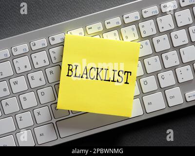 The word blacklist written on a sticky note paper on computer keyboard. Blocking spam messages, calls or unwanted people. Stock Photo
