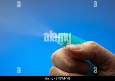 Small spray bottle pulverizer nozzle macro held by Caucasian male hand. Close up studio shot, isolated on blue background. Stock Photo