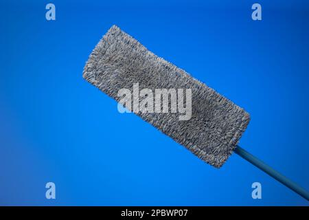 Generic plastic sweeping mop with a dirty textile sponge. Close up studio shot, isolated on blue background. Stock Photo
