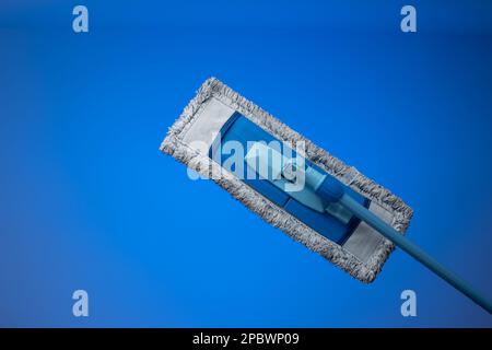 Generic plastic sweeping mop with a dirty textile sponge. Close up studio shot, isolated on blue background. Stock Photo