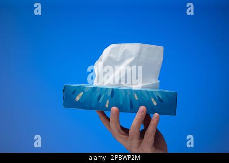Paper tissue dispenser held by Caucasian male hand. Close up studio shot, isolated on blue background. Stock Photo